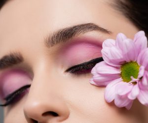 cropped view of sensual young woman with pink eye shadows holding flower