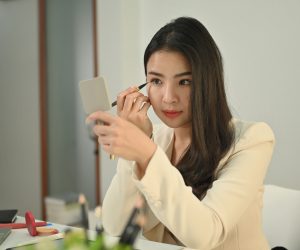 Attractive young businesswoman in stylish suit is making up on w